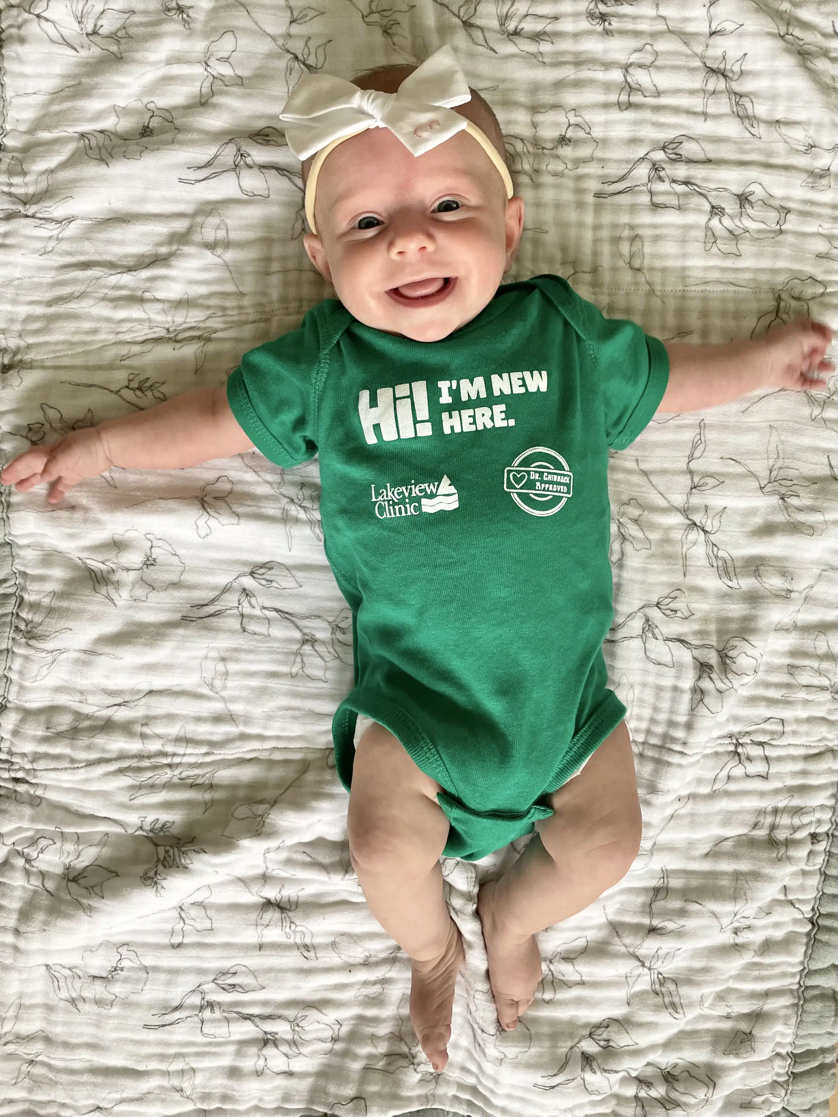 New baby Elsie Bussler.8.16.25 Green Lakeview onesie on blue background.